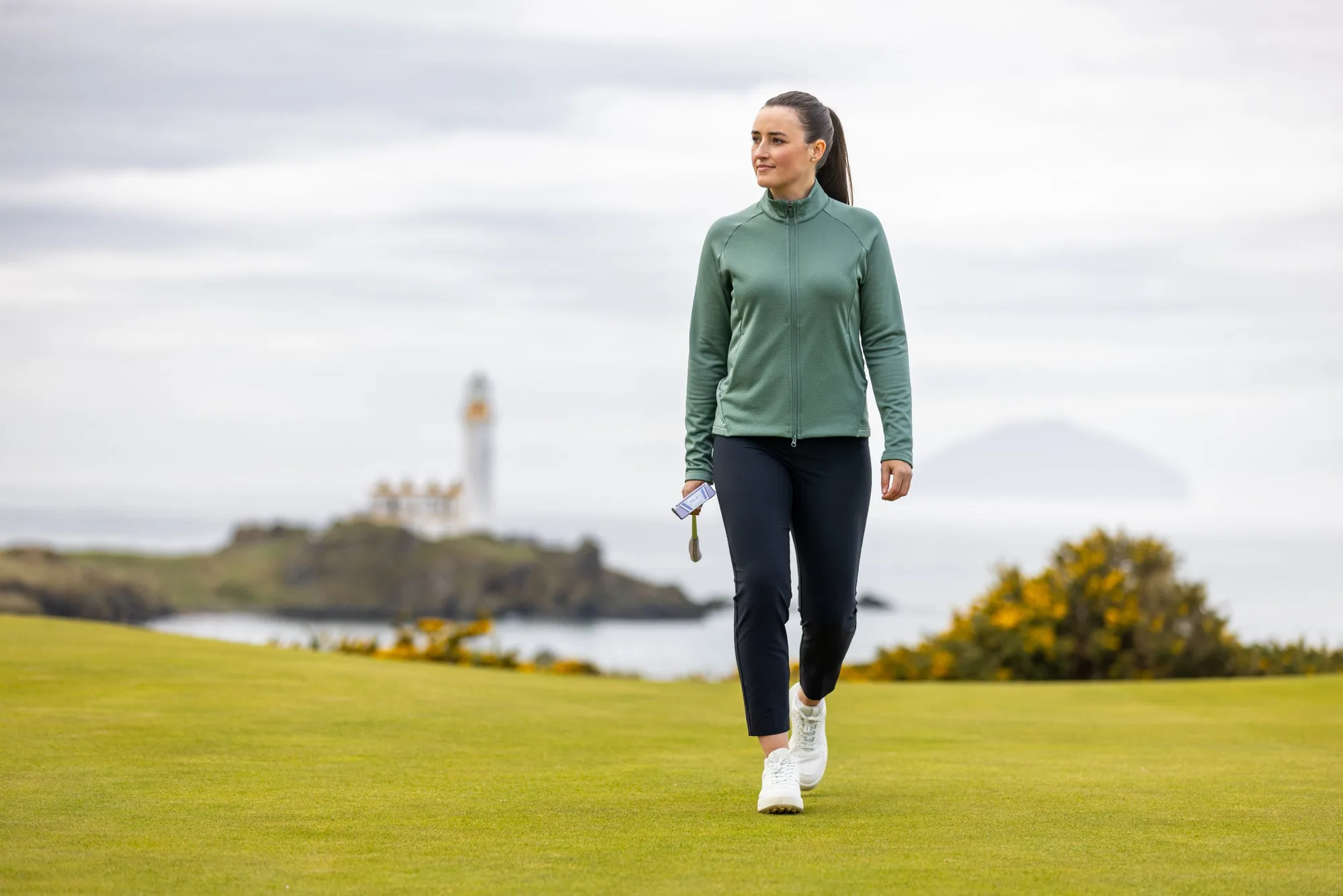 Jae Bowers walking down a fairway at Turnberry with the lighthouse behind her