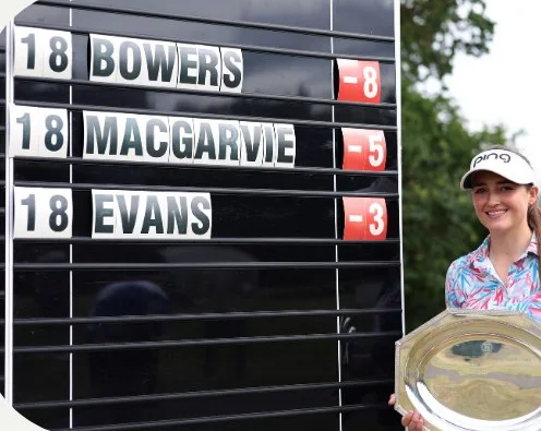 Jae Bowers with the WPGA Championship trophy beside a leaderboard showing her on −8