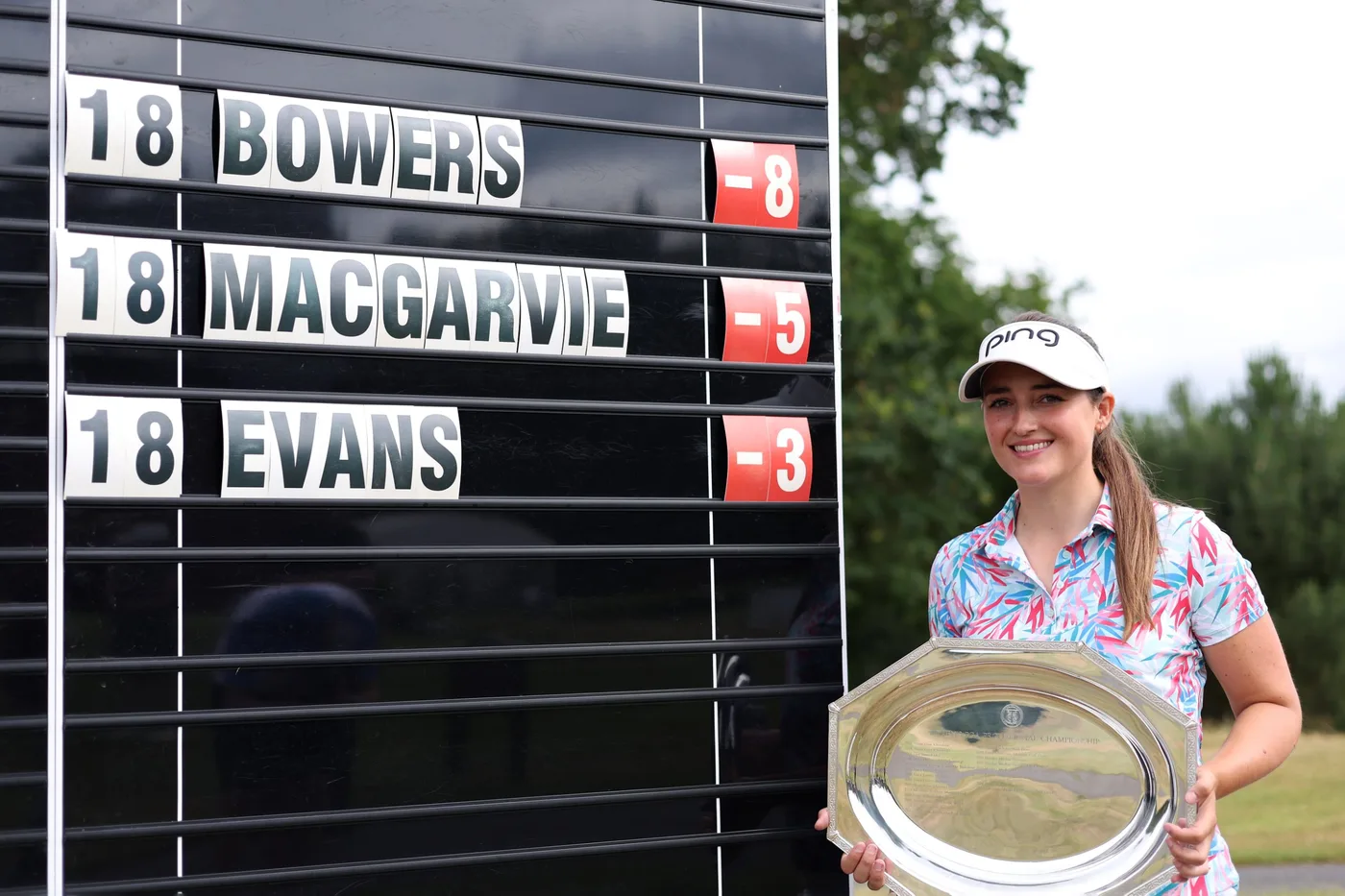 Jae Bowers holding the WPGA Professional Championship trophy beside the leaderboard showing her winning on −8